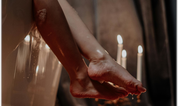 Pernas de mulher molhadas sentadas numa banheira com velas ao fundo para mostrar o que é chuva dourada.